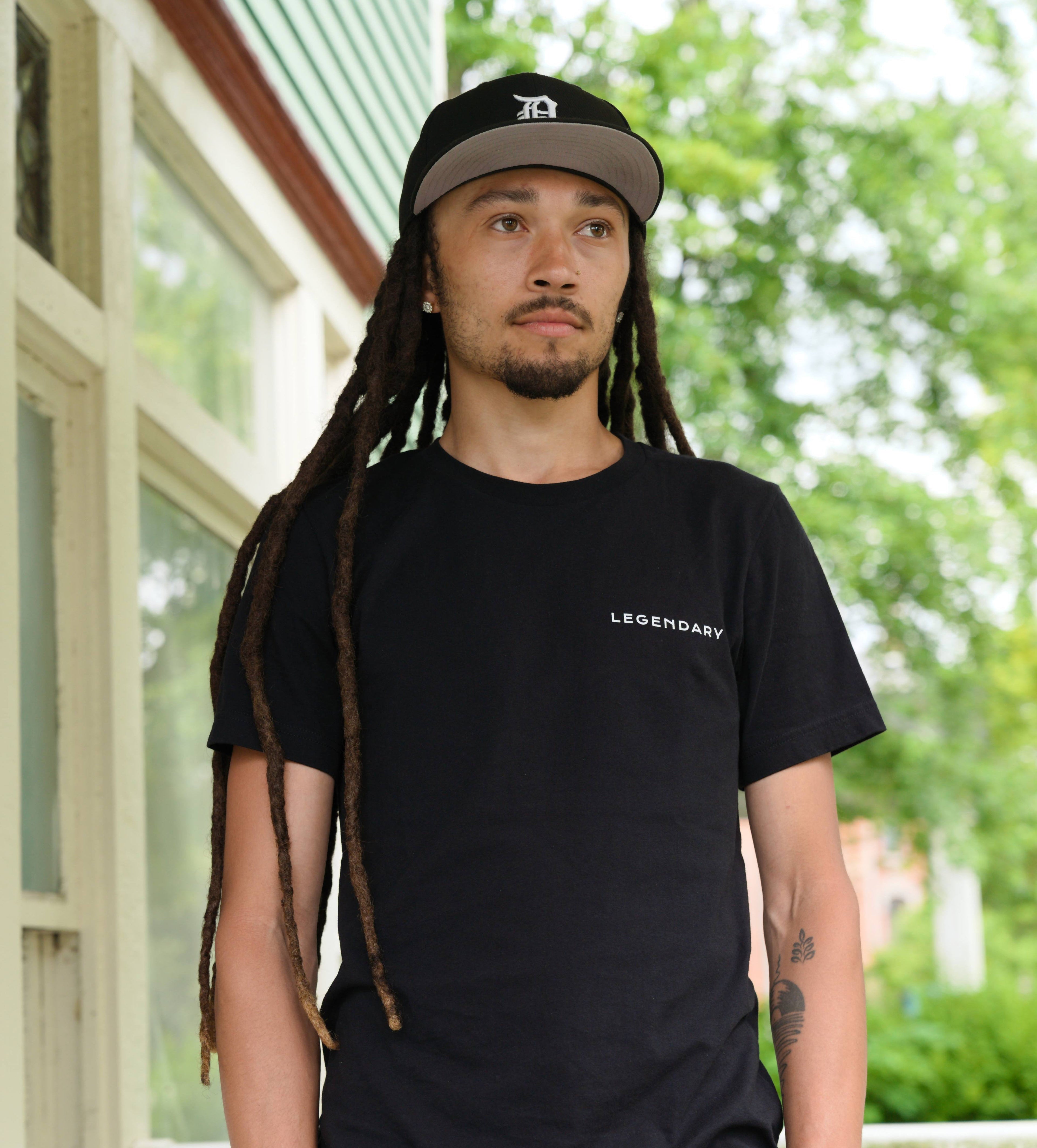 Person wearing a black t-shirt with 'LEGENDARY' text, standing outdoors.